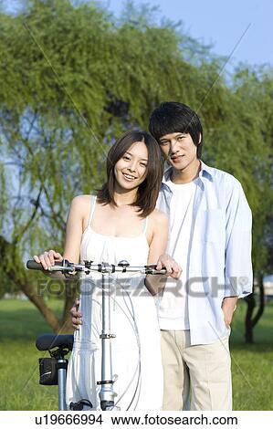 Picture - Young couple standing on the lawn with a bicycle. Fotosearch