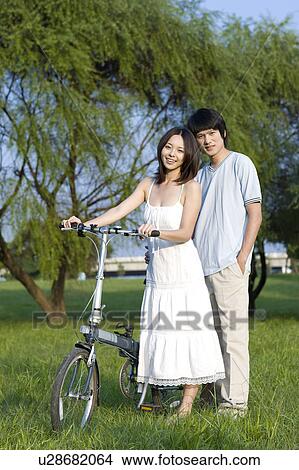 Young couple standing on the lawn with a bicycle View Large Photo Image Picture - Young couple standing on the lawn with a bicycle. Fotosearch