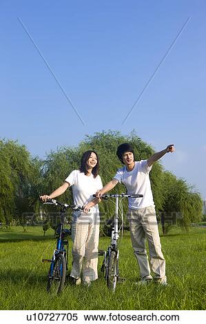 Young couple standing on the lawn with bicycles, looking away View Large Photo Image Stock Photography - Young couple standing on the lawn with bicycles, looking away. Fotosearch