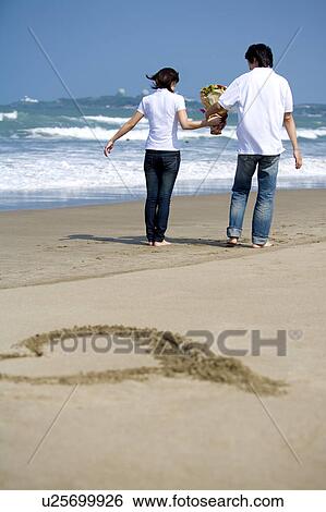 Young couple walking on the beach and holding a bunch of flowers View Large Photo Image Stock Photograph - Young couple walking on the beach and holding a bunch of flowers. Fotosearch
