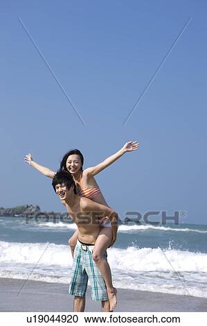 Stock Image - Young woman on the young man's back with arms outstretched. Fotosearch