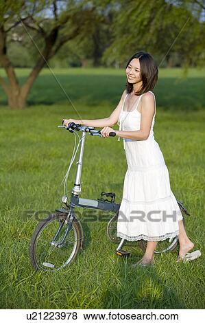 Stock Photo - Young woman walking on the lawn with a bicycle. Fotosearch