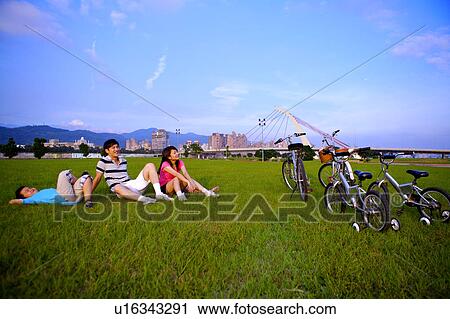 Stock Image - Family with one child sitting and lying on the lawn, looking up. Fotosearch