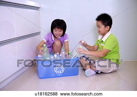 Stock Photo - Little boy and girl sitting on the floor and putting empty bottles into recycling bin. Fotosearch