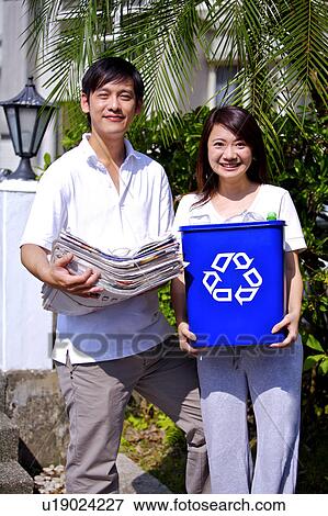 Young couple holding a stack of newspaper and recycling bin, looking at the camera and smiling happily View Large Photo Image Stock Photo - Young couple holding a stack of newspaper and recycling bin, looking at the camera and smiling happily. Fotosearch