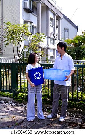Stock Image - Young couple holding the recycling bins and smiling at each other. Fotosearch