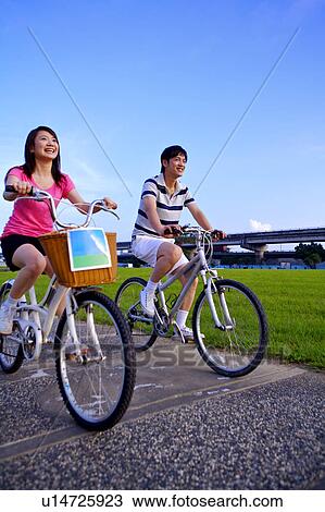 Young couple riding on bicycles and looking away by river bank View Large Photo Image Stock Image - Young couple riding on bicycles and looking away by river bank. Fotosearch