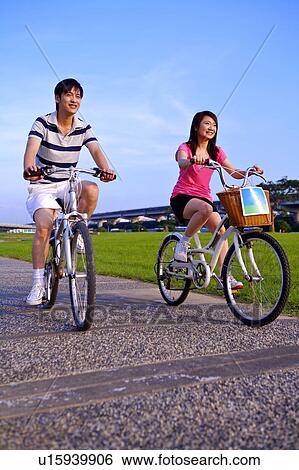 Young couple riding on the bicycle, looking away and smiling View Large Photo Image Stock Photograph - Young couple riding on the bicycle, looking away and smiling. Fotosearch