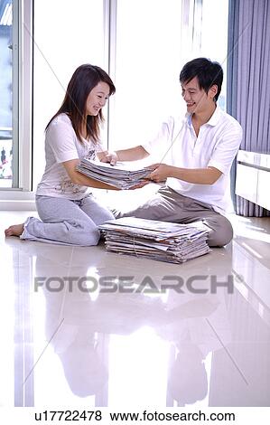 Young couple sitting on the floor and packing up the newspaper, smiling happily View Large Photo Image Stock Photo - Young couple sitting on the floor and packing up the newspaper, smiling happily. Fotosearch