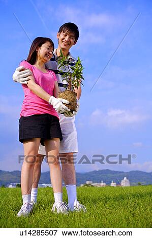 Young couple standing on the lawn, holding a plant and smiling happily View Large Photo Image Stock Photo - Young couple standing on the lawn, holding a plant and smiling happily. Fotosearch