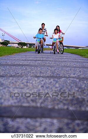 Stock Image - Young family with two children riding on the bicycle and smiling happily. Fotosearch