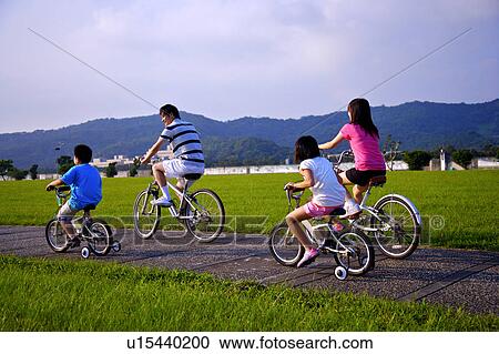 Stock Image - Young family with two children riding on the bicycles together. Fotosearch