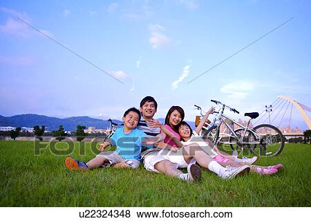 Stock Photo - Young family with two children sitting on the lawn together and smiling happily. Fotosearch