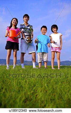 Stock Image - Young family with two children standing on the lawn, holding tools for planting and looking at the camera. Fotosearch