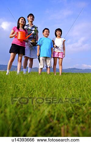 Young family with two children standing on the lawn, looking away and smiling View Large Photo Image Stock Photograph - Young family with two children standing on the lawn, looking away and smiling. Fotosearch