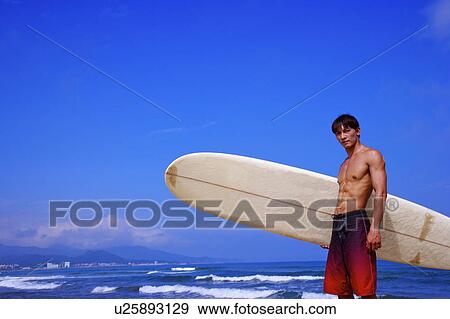 Man holding the surfboard and looking at the camera View Large Photo Image Stock Photo - Man holding the surfboard and looking at the camera. Fotosearch