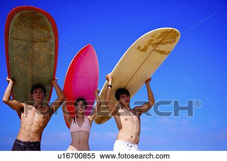 Stock Photography - Three people carrying the surfboards on heads and looking away. Fotosearch