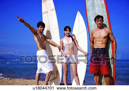 Stock Image - Three people holding the surfboards and looking at the camera. Fotosearch