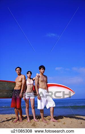 Three people standing on beach with surfboards and looking at the camera View Large Photo Image Stock Photo - Three people standing on beach with surfboards and looking at the camera. Fotosearch