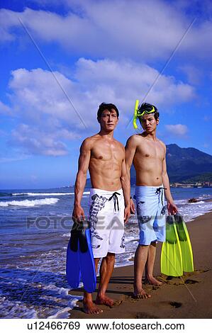 Stock Photo - Two man holding the flippers, standing on the beach and looking away. Fotosearch