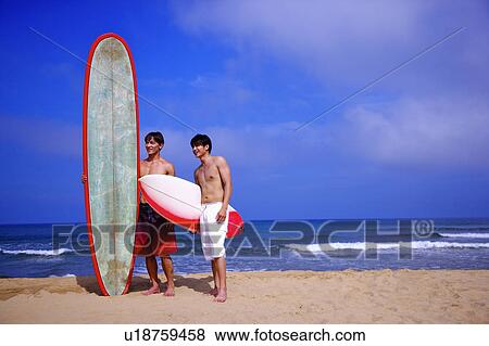Stock Photo - Two men holding surfboards on beach and looking away. Fotosearch