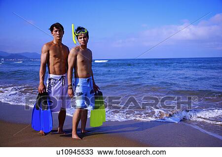 Stock Image - Two men holding the flippers, wearing the swimming goggles and looking at the camera. Fotosearch