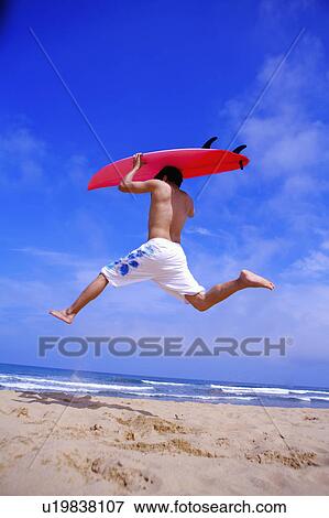 Young man carrying a surfboard on head, jumping up mid-air View Large Photo Image Stock Photo - Young man carrying a surfboard on head, jumping up mid-air. Fotosearch
