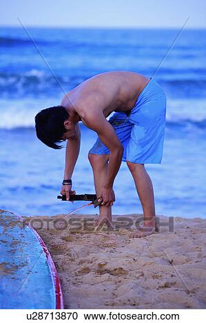 Stock Image - Young man standing on beach and tying. Fotosearch