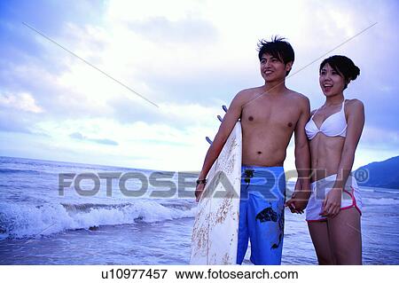 Stock Photo - Young woman and young man standing together and holding hands. Fotosearch
