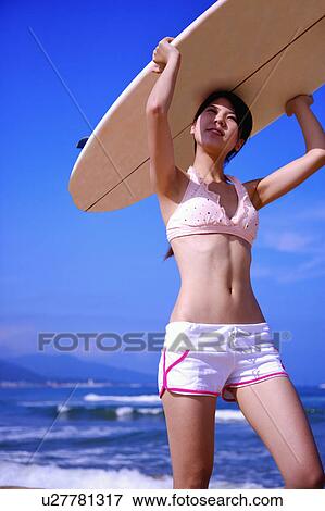Stock Photo - Young woman carrying the surfboard on head and looking up. Fotosearch