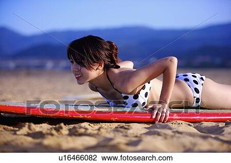 Stock Image - Young woman lying on the surfboard on front and practicing. Fotosearch