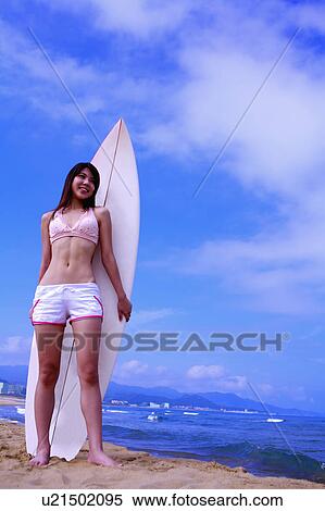 Young woman standing in front of surfboard on beach and looking away View Large Photo Image Stock Photography - Young woman standing in front of surfboard on beach and looking away. Fotosearch