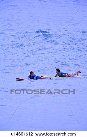 Stock Image - Man and young woman floating on the sea with the surfboard. Fotosearch