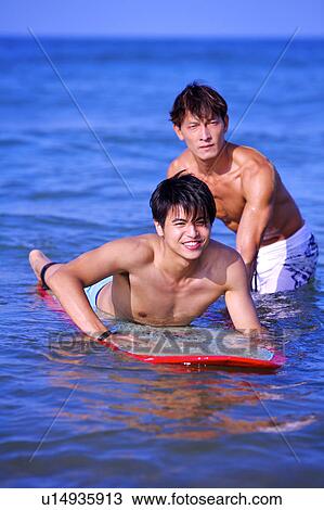 Stock Image - Man helping young man floating on the sea with the surfboard. Fotosearch