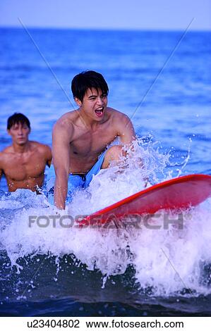Stock Image - Man helping young man surfing on the sea. Fotosearch