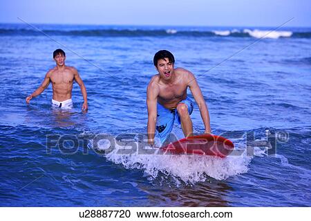 Stock Image - Man helping young man surfing on the sea. Fotosearch