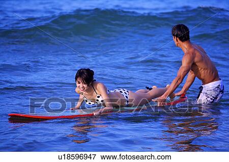 Stock Photo - Man helping young woman floating on the sea with the surfboard. Fotosearch