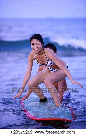 Stock Photo - Man helping young woman surfing on the sea. Fotosearch