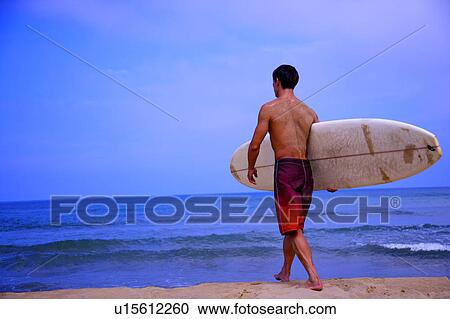 Stock Image - Man holding the surfboard and walking toward the sea. Fotosearch