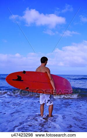 Man standing in the water and holding the surfboard View Large Photo Image Stock Photo - Man standing in the water and holding the surfboard. Fotosearch