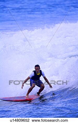 Stock Image - Man surfing on the sea skillfully with huge surf behind. Fotosearch
