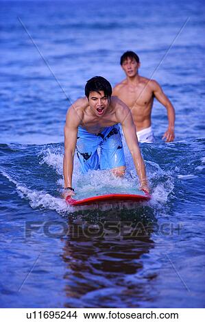 Picture - Man teaching young man surfing on the sea. Fotosearch