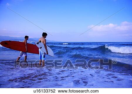Two men holding the surfboards and standing in the sea View Large Photo Image Stock Image - Two men holding the surfboards and standing in the sea. Fotosearch