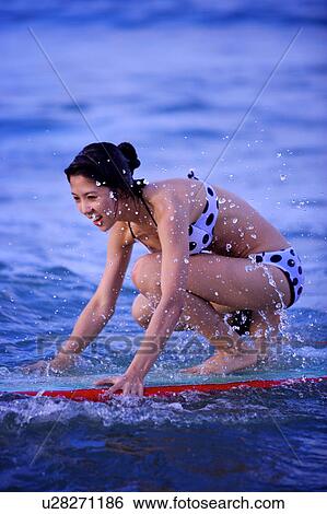 Stock Photograph - Woman floating on the sea with the surfboard and smiling happily. Fotosearch