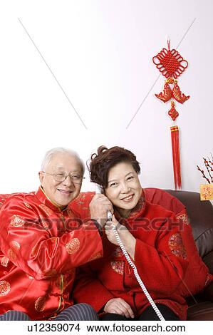 Elderly couple in traditional clothes sitting on the sofa, on the phone View Large Photo Image Picture - Elderly couple in traditional clothes sitting on the sofa, on the phone. Fotosearch