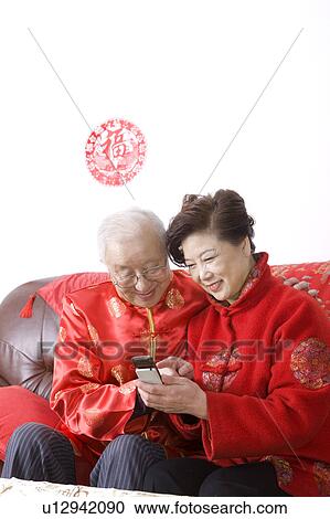Elderly couple in traditional clothes sitting on the sofa and looking at the mobile phone together View Large Photo Image Stock Image - Elderly couple in traditional clothes sitting on the sofa and looking at the mobile phone together. Fotosearch