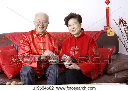 Stock Image - Elderly couple in traditional clothes holding tea cups and smiling at the camera. Fotosearch