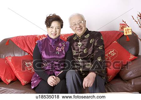 Stock Photo - Elderly couple in traditional clothes sitting on the sofa and smiling at the camera. Fotosearch