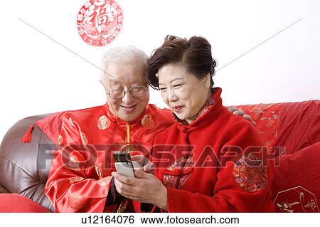 Elderly couple in traditional clothes sitting on the sofa and looking at the mobile phone together View Large Photo Image Stock Photograph - Elderly couple in traditional clothes sitting on the sofa and looking at the mobile phone together. Fotosearch