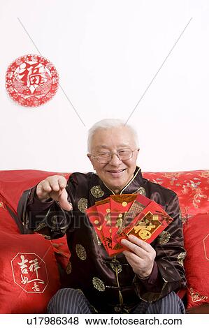 Stock Photo - Elderly man in traditional clothes holding red envelopes and smiling at the camera. Fotosearch